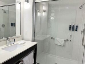 A modern bathroom with a glass-enclosed shower, a large mirror, and a countertop with a sink and toiletries. - Four Points By Sheraton Edmonton Gateway (Edmonton)