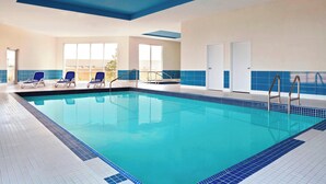 Una piscina interior con agua azul cristalina, paredes con azulejos azules y algunas sillas de descanso.