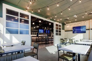 A modern restaurant interior with multiple tables and chairs, large windows, and a bar area. - Four Points By Sheraton Edmonton Gateway (Edmonton)