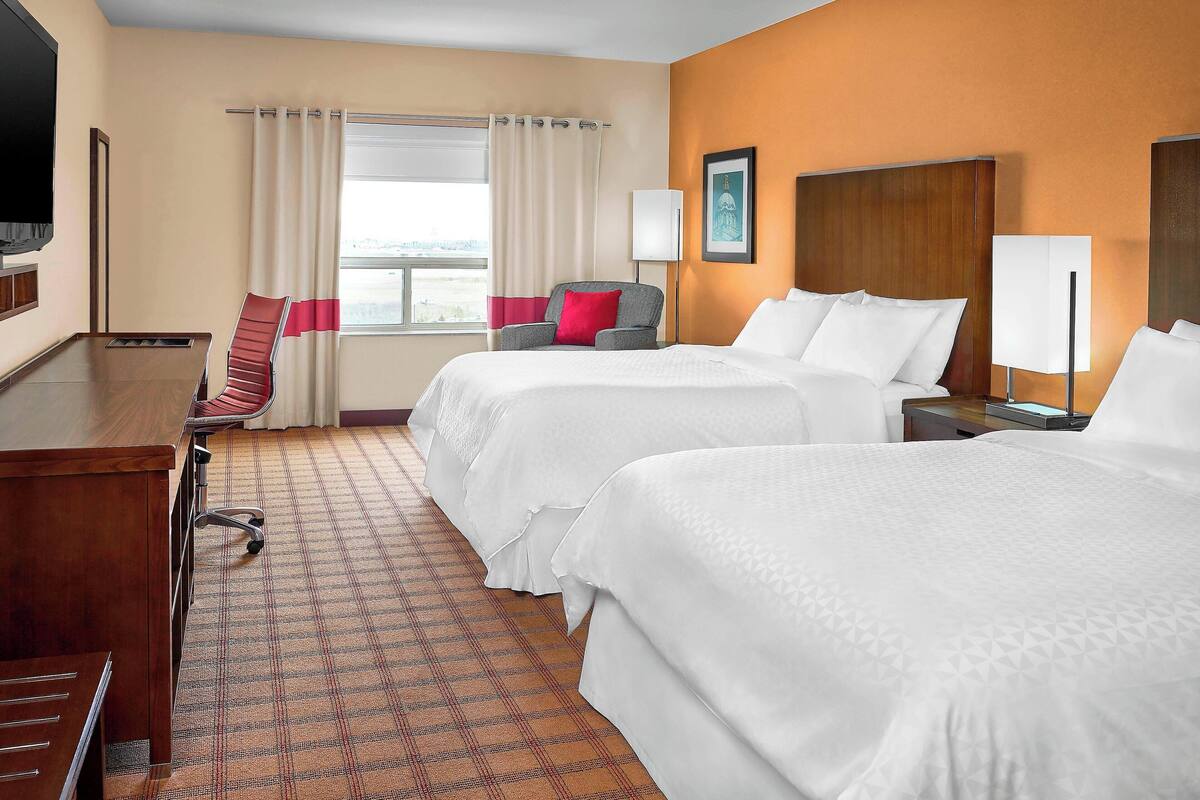 Una habitación de hotel con dos camas, un escritorio, una silla, un televisor y una ventana con cortinas.