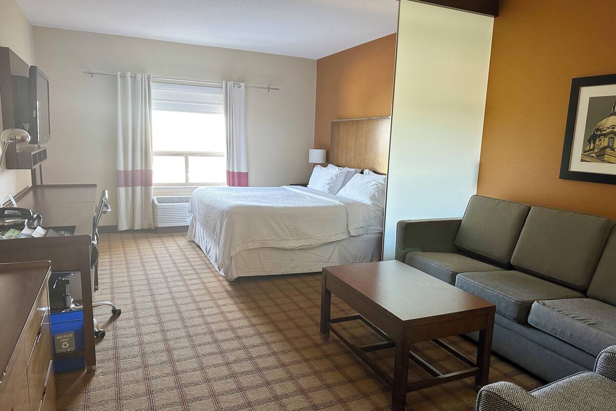 Una habitación de hotel con cama, sofá, escritorio y ventana con cortinas.