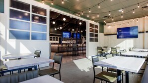 Un restaurante moderno con varias mesas y sillas, una zona de bar y ventanas amplias.
