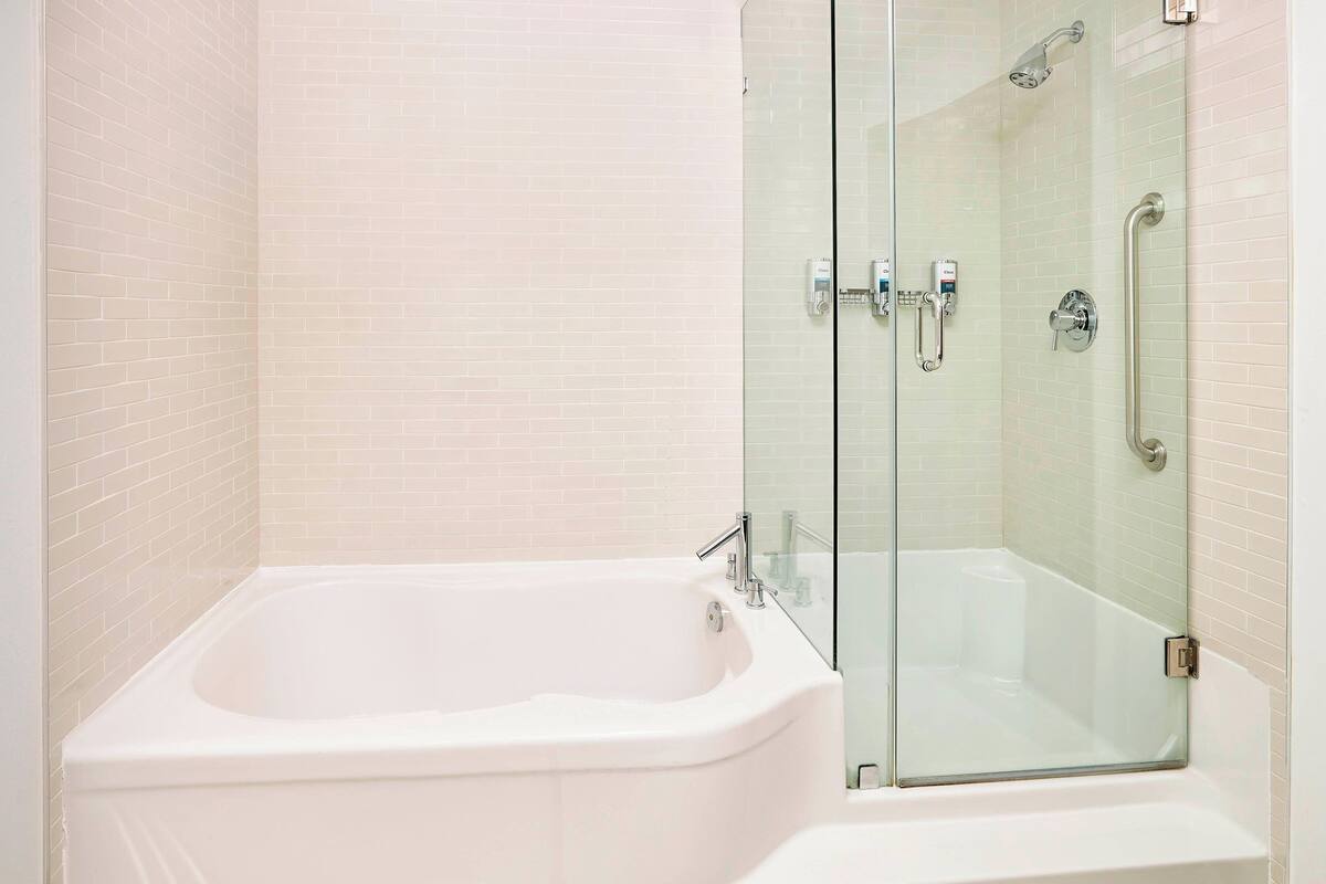 Un baño moderno con una bañera blanca, cabina de ducha de vidrio y pared con azulejos.
