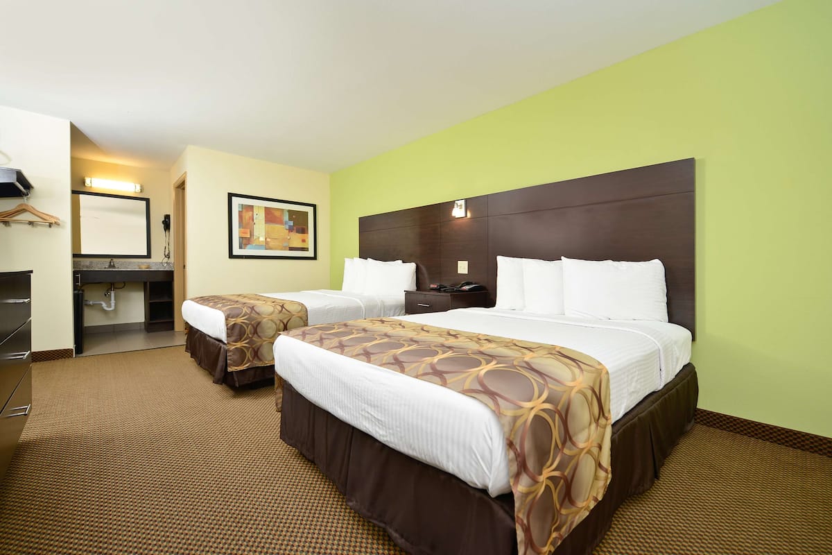 A hotel room with two beds, a bathroom, and a small desk area.