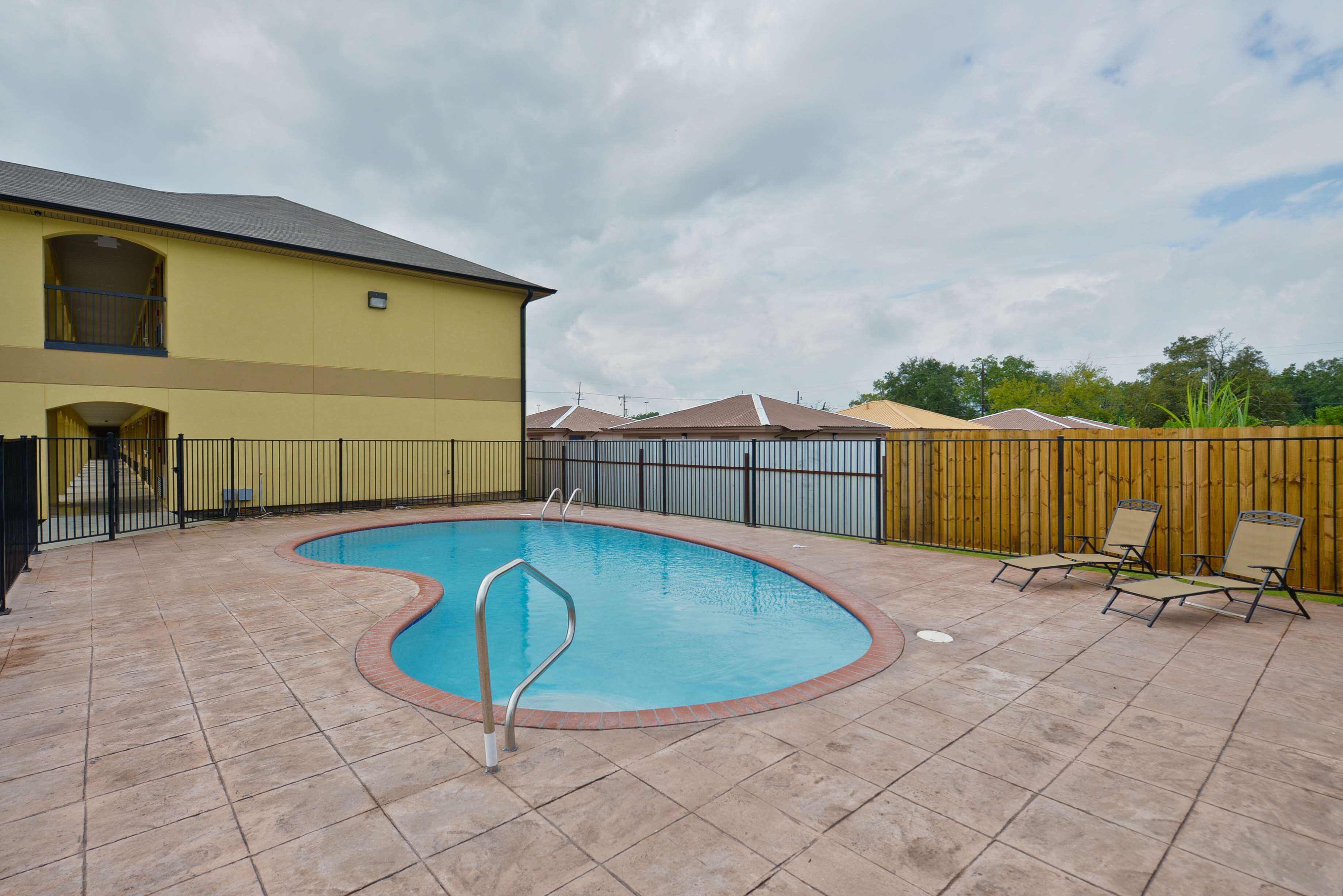 A backyard with a swimming pool, a wooden fence, and a building with a balcony.