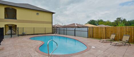 A backyard with a swimming pool, a wooden fence, and a building with a balcony.