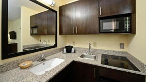 A modern bathroom with dark wood cabinets, a granite countertop, a double sink, a mirror, and a built-in microwave.