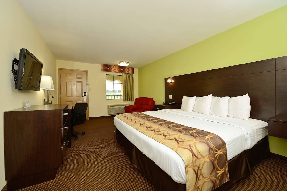 A hotel room with a large bed, a desk with a chair, a red chair, a television, and a window with a view.