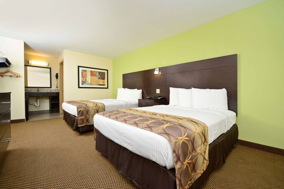 A hotel room with two beds, a desk, a chair, a mirror, and a painting on the wall.
