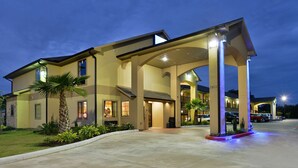 A hotel with a covered entrance, palm trees, and a parking lot at dusk.