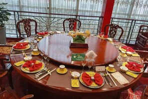 Mesa redonda posta para refeição, com cadeiras ao redor, um suporte para menu e um arranjo decorativo.