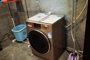 A compact, wall-mounted washing machine with a control panel, a blue laundry basket, and a metal hose. - Fuling Hotel (Chongqing)