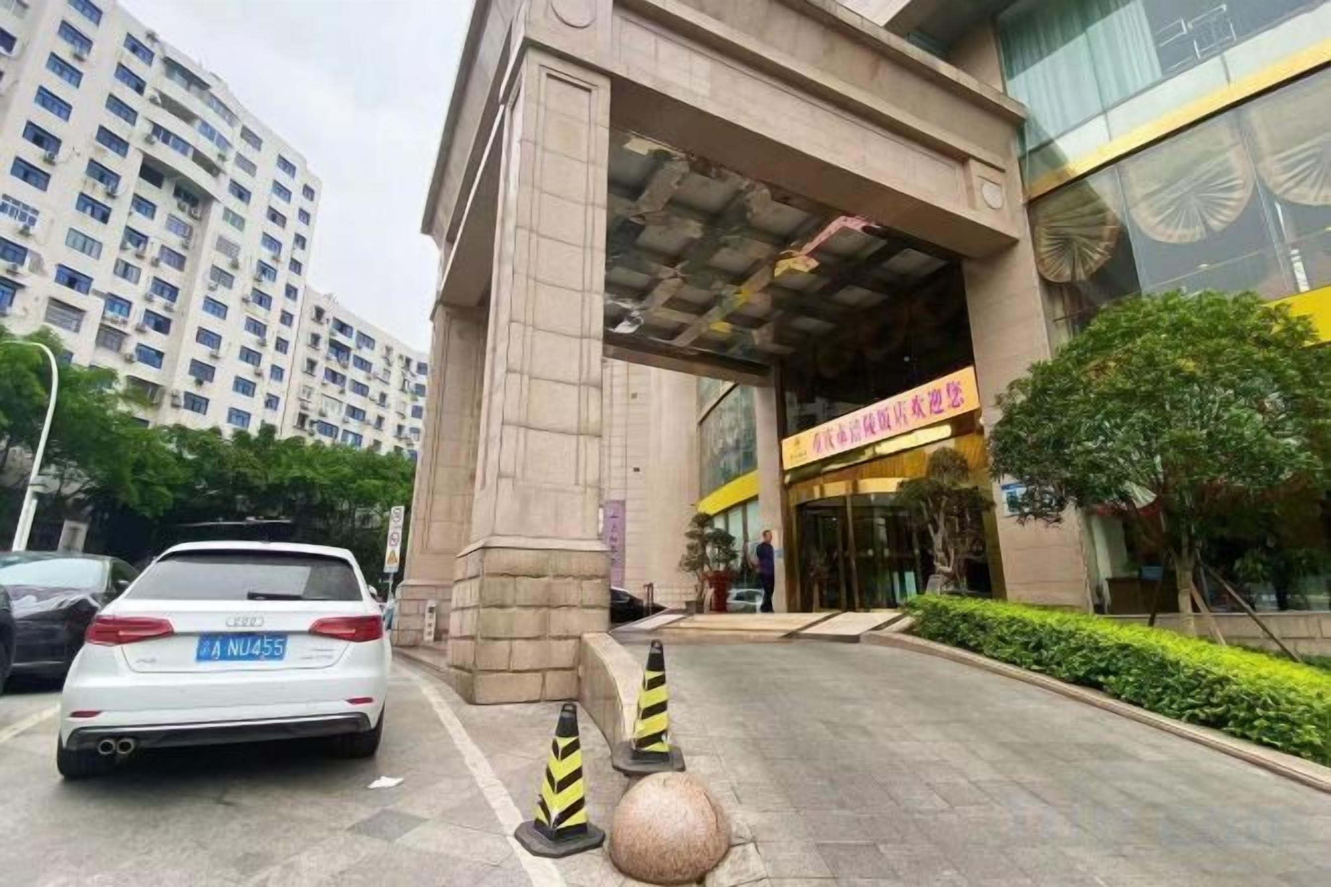 A hotel entrance with a large overhang, a car parked in front, and a building with a sign in the background.