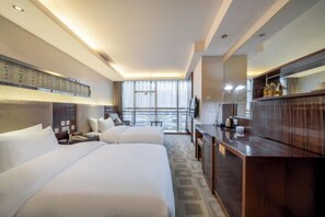 A hotel room with two beds, a desk, a TV, and a large window.