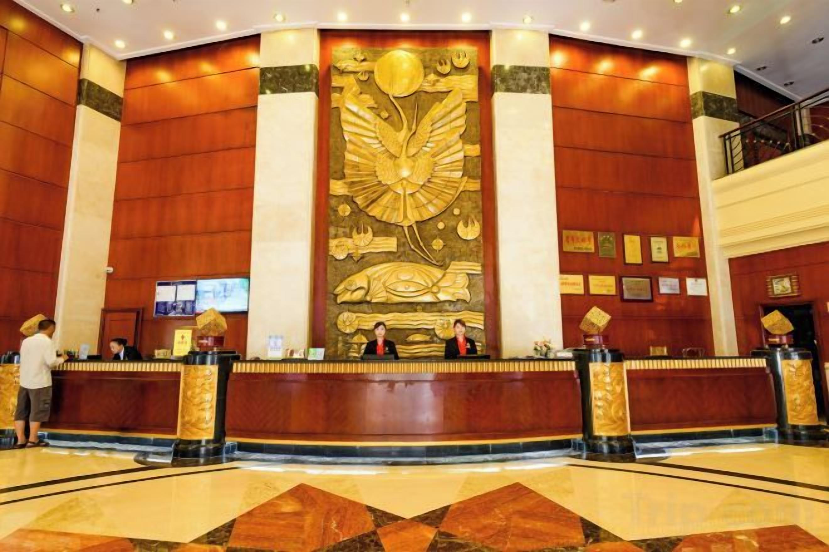 A hotel reception area with a large decorative wall, reception desk, and a polished floor.