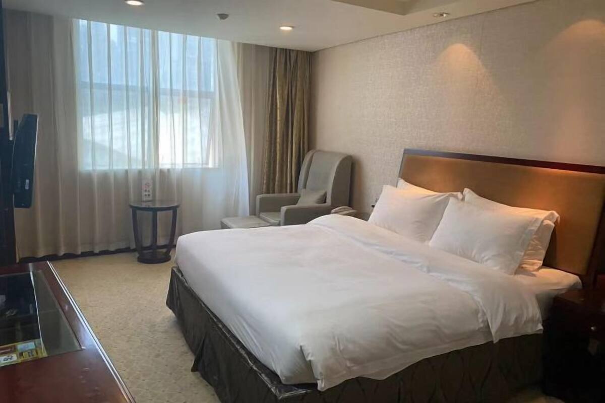 A hotel room with a large bed, a chair, a TV, and a window with curtains.