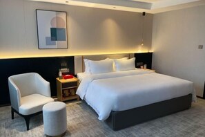 A modern hotel room with a large bed, a chair, a small table, and a bedside lamp.
