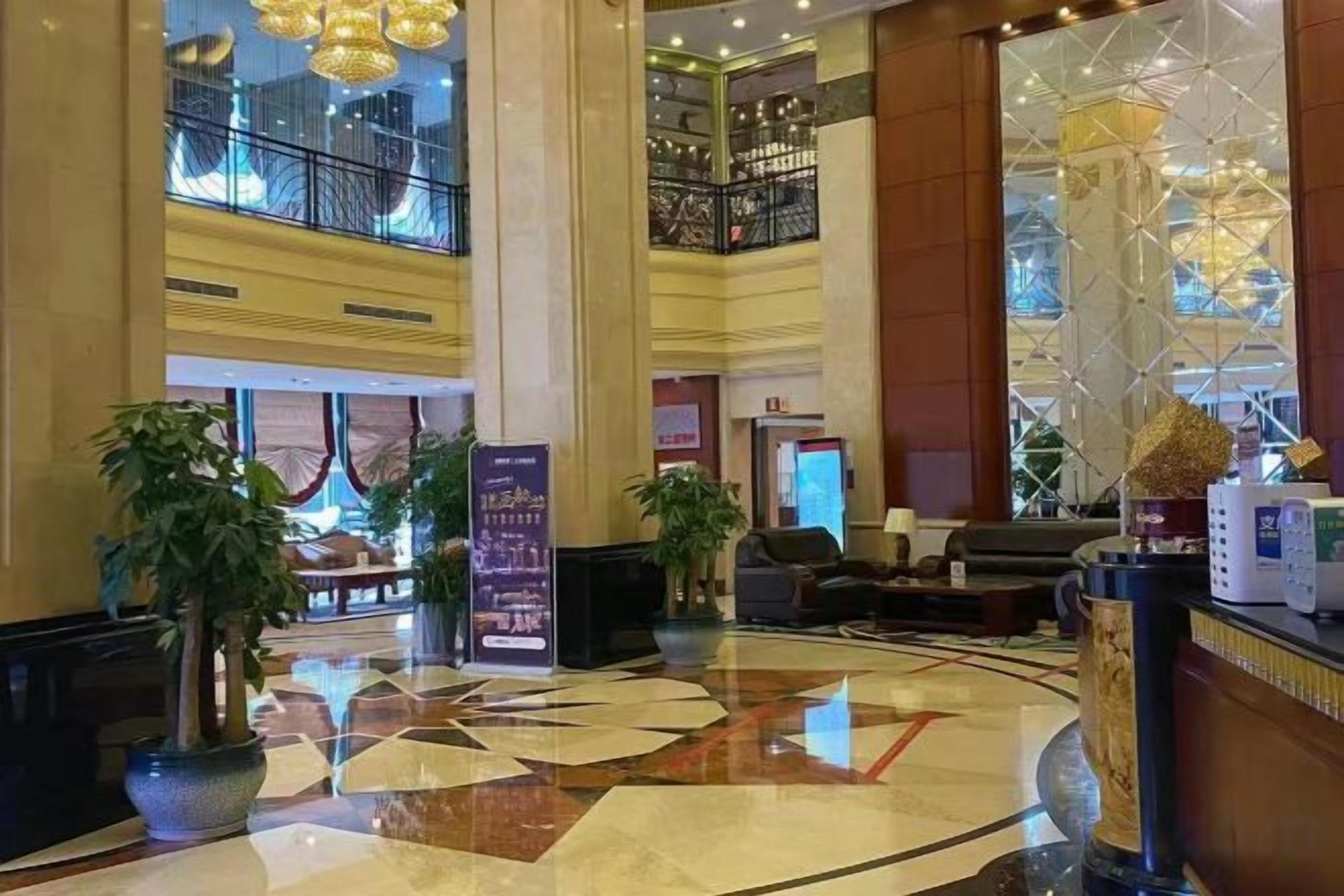 A hotel lobby with a high ceiling, large columns, a check-in counter, seating area, and a staircase leading to an upper level.