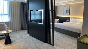 Une chambre d’hôtel avec un lit, un téléviseur fixé sur un panneau noir, une petite table ronde et un canapé.