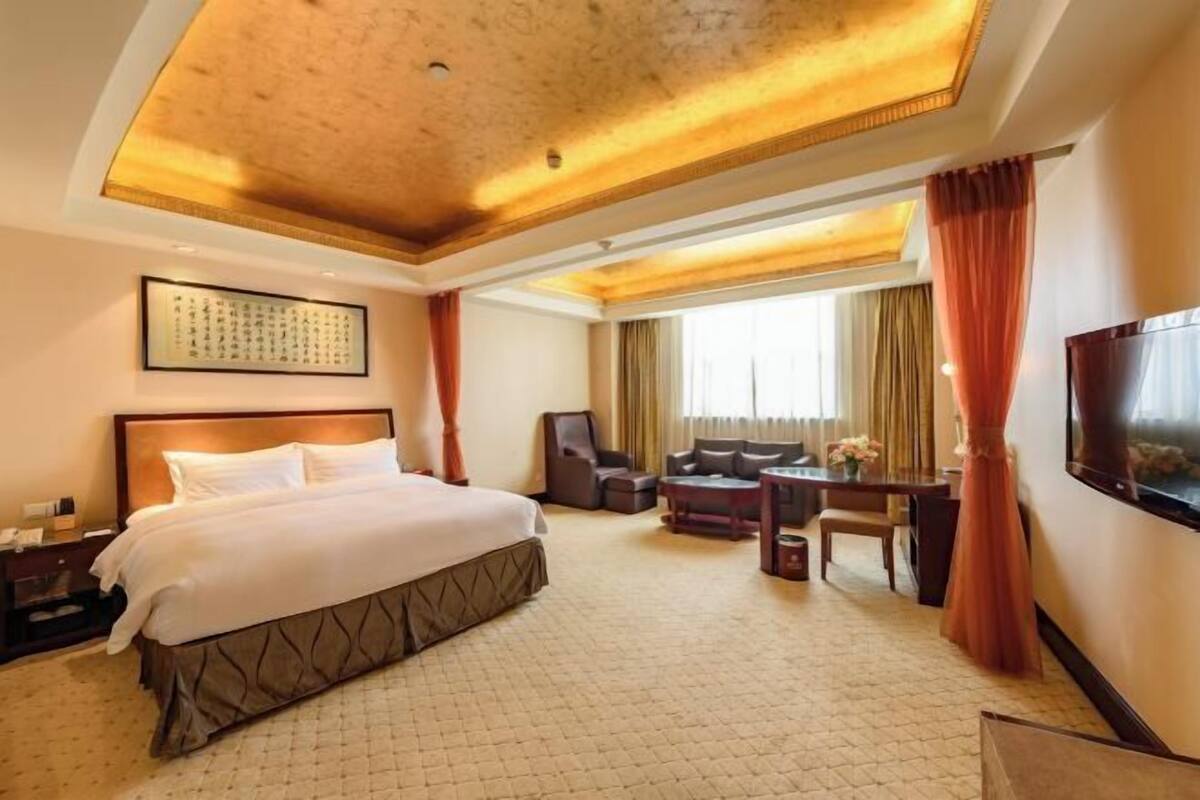 A hotel room with a large bed, a desk, a chair, and a TV.