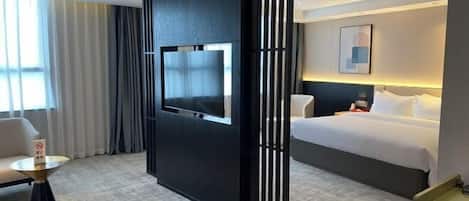 A hotel room with a bed, a TV mounted on a black partition, a round table, and a chair.