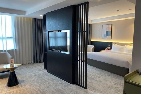 A hotel room with a bed, a TV mounted on a black partition, a round table, and a chair. - Fuling Hotel (Chongqing)
