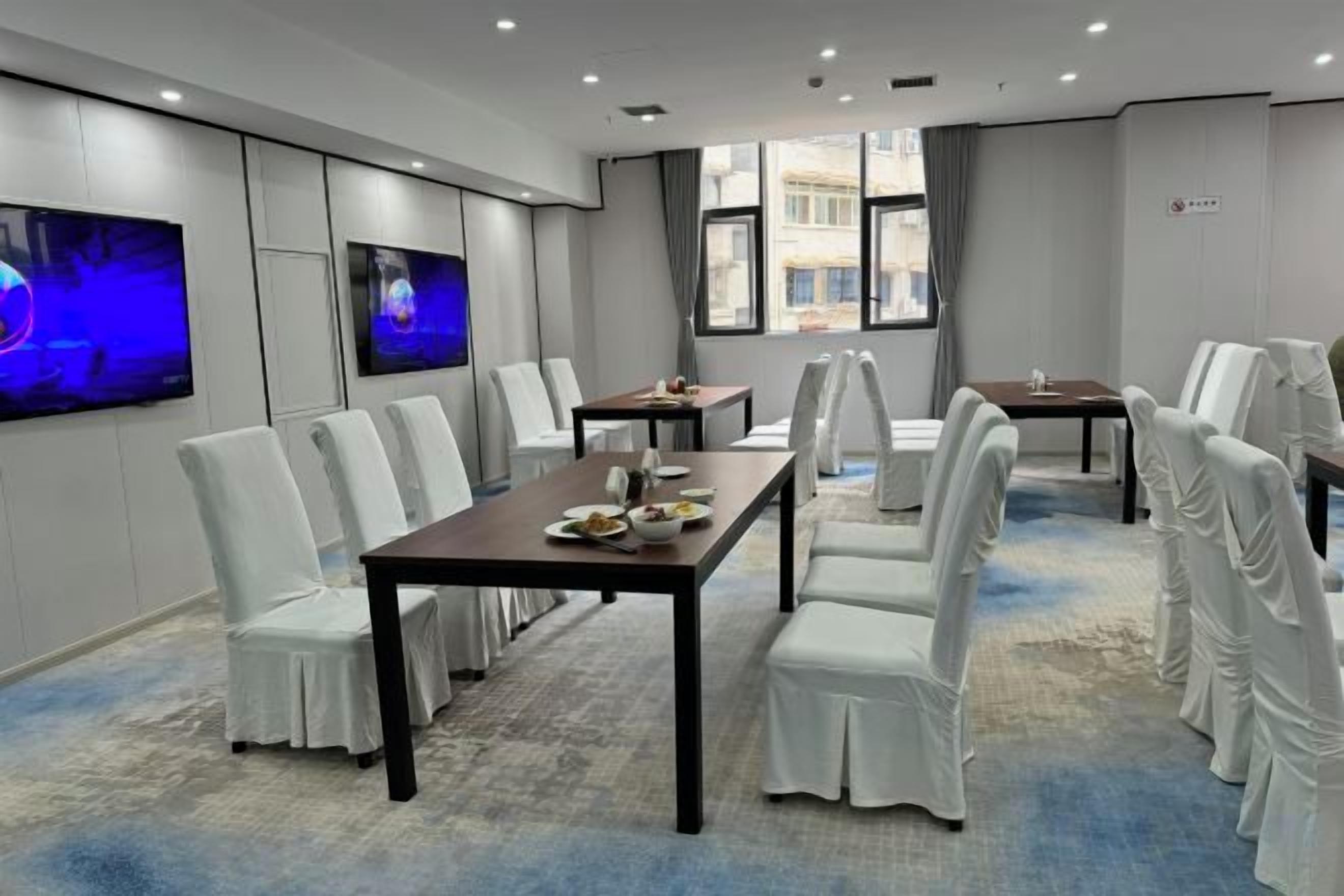 A conference room with a long table, white chairs, and a television screen.