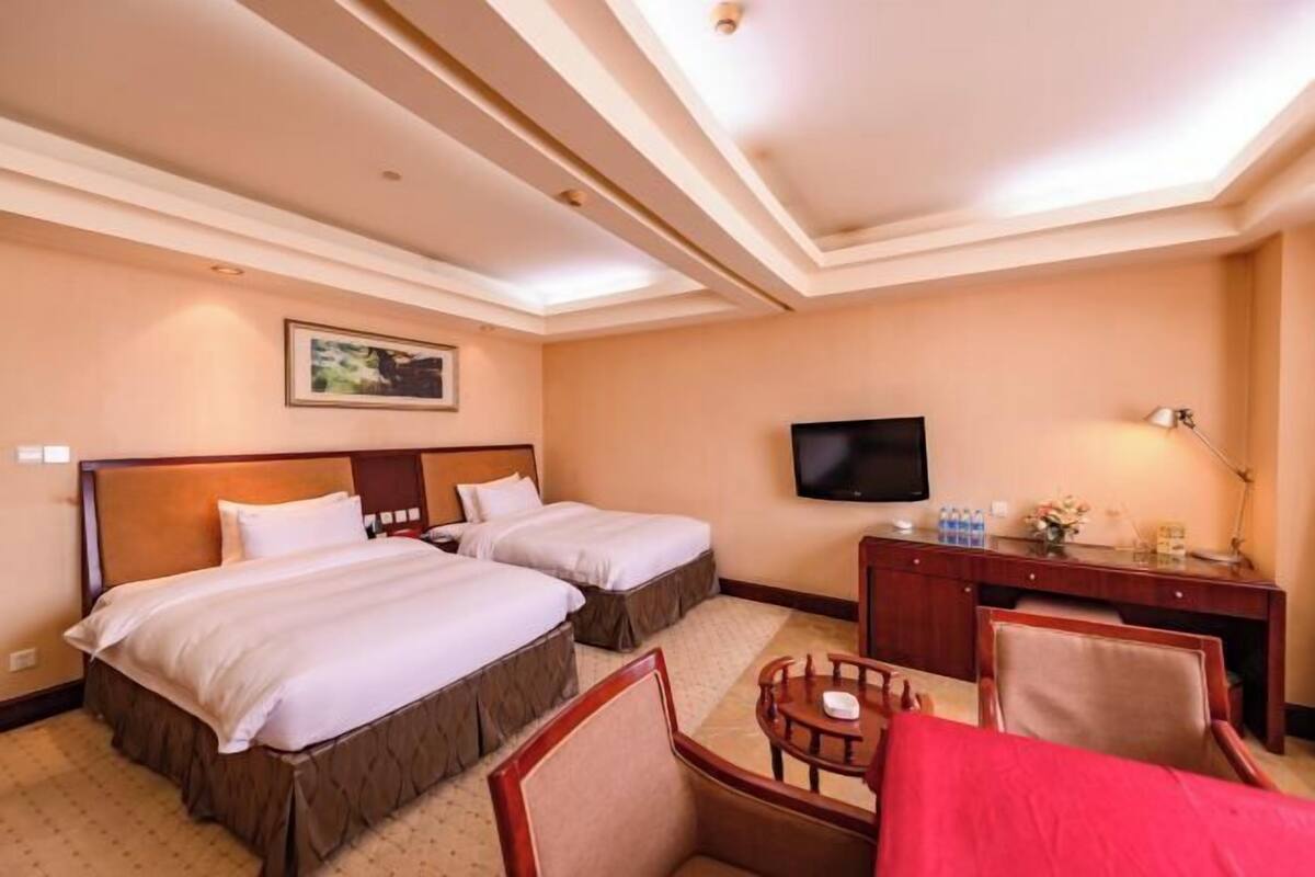 A hotel room with two beds, a desk, a TV, and a small seating area.