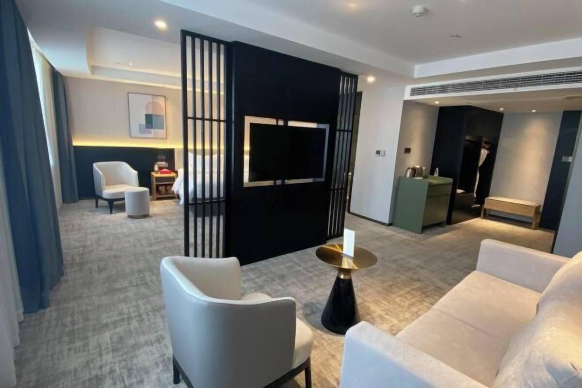 A modern hotel room with a large flat-screen TV, a sofa, a chair, and a decorative table.
