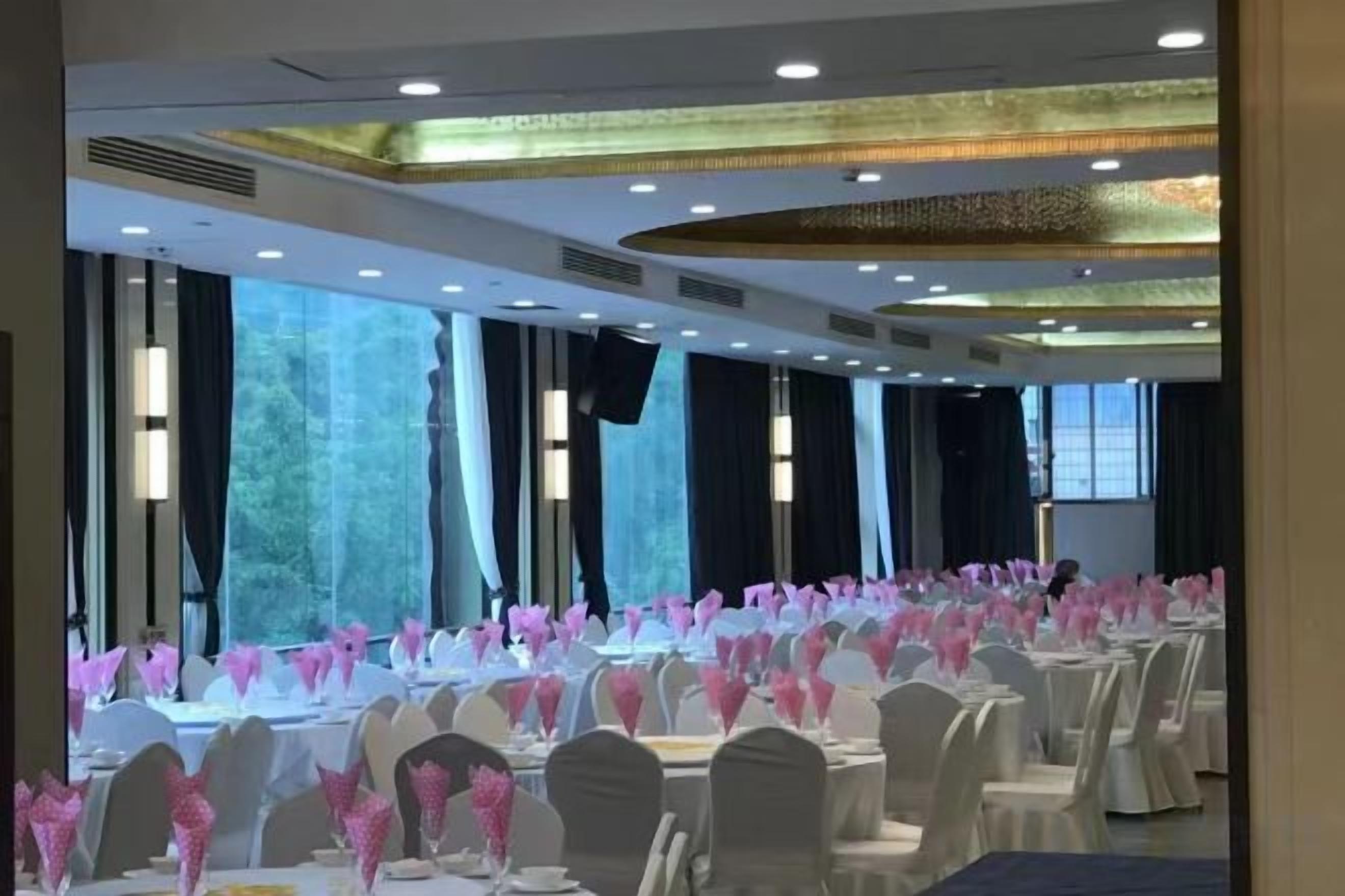 A banquet hall with round tables, chairs, and pink floral centerpieces.