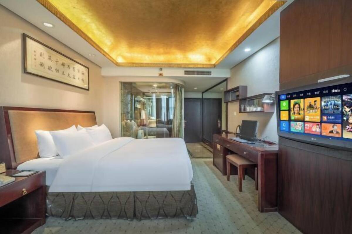 A hotel room with a bed, desk, TV, and a framed picture on the wall.