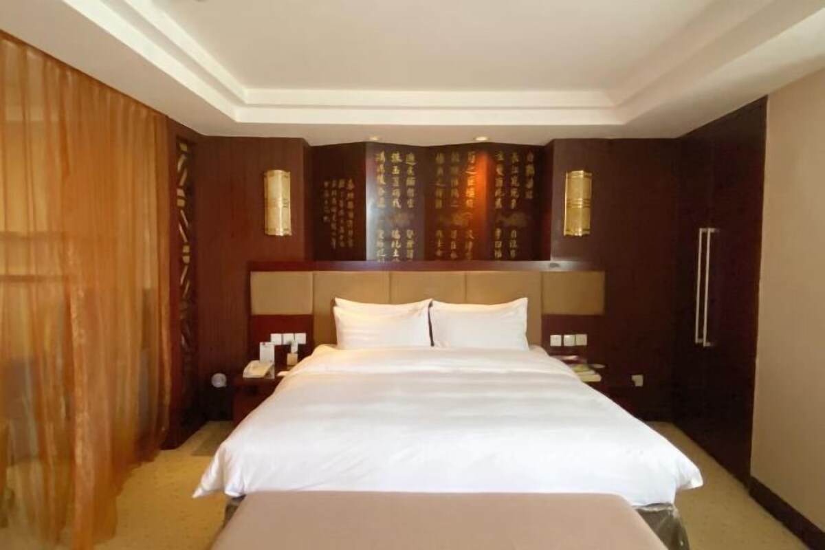 A hotel room with a large bed, a wooden headboard, a nightstand, and a wall with decorative panels.
