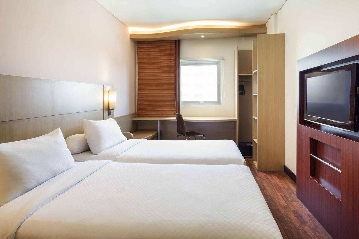Een hotelkamer met twee bedden, een bureau, een televisie en een kledingkast.