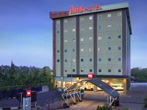 A multi-story hotel with a prominent 'ibis HOTEL' sign, a covered entrance, and a visible outdoor area with plants. - ibis Balikpapan (Balikpapan)