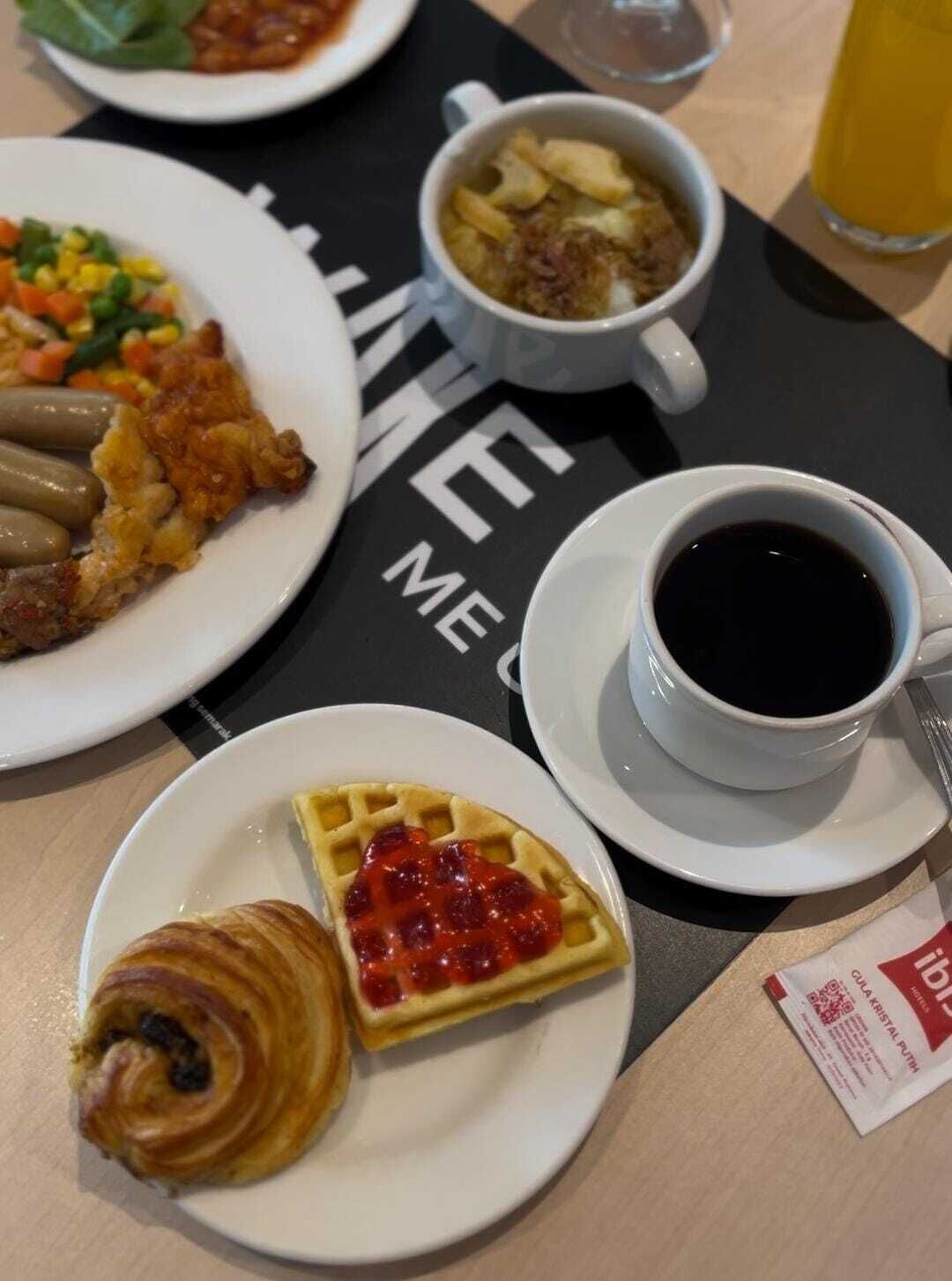 A breakfast setting with a waffle, croissant, coffee, and a bowl of soup on a table.