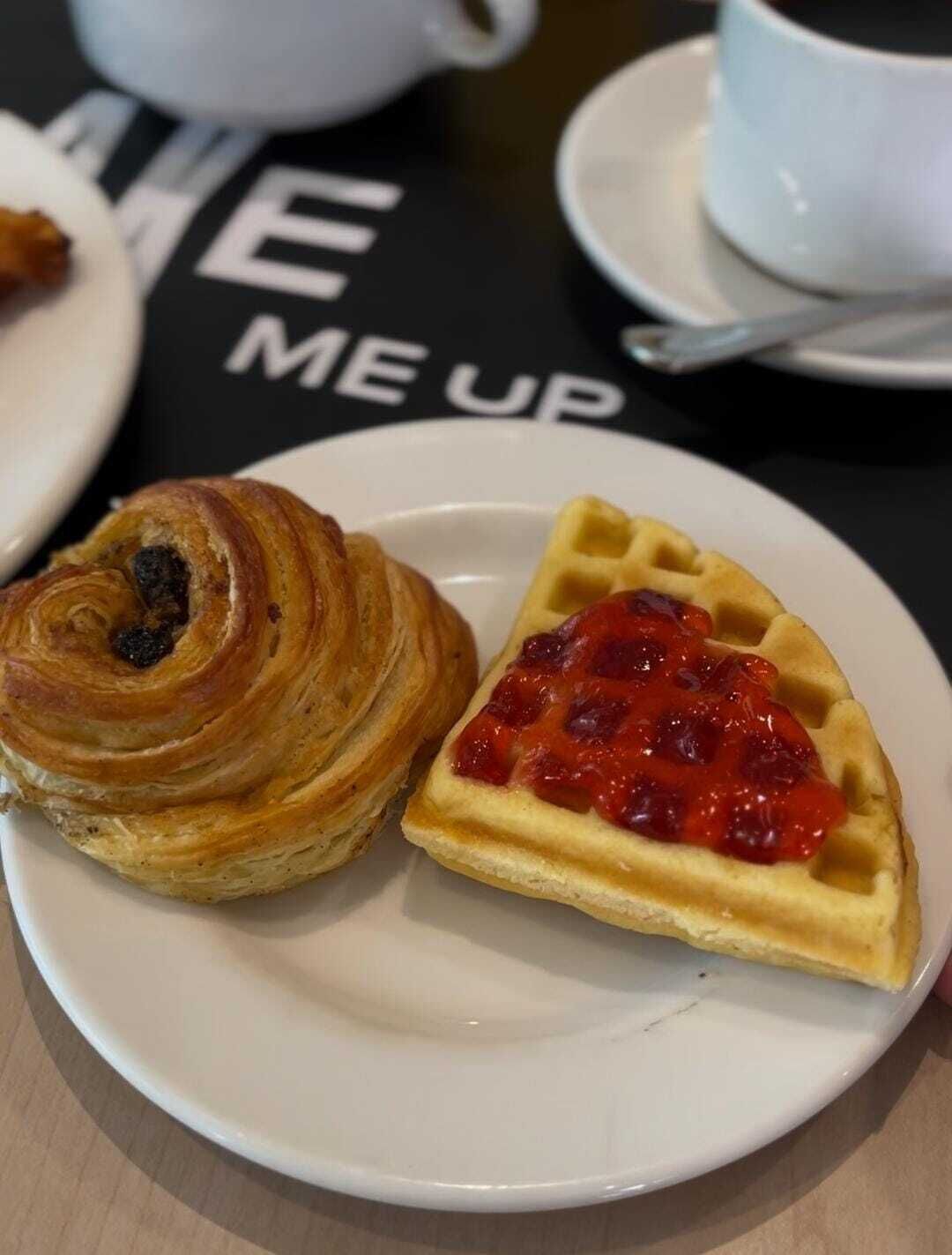 A plate with a croissant and a waffle topped with red fruit compote.