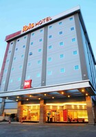 Un hotel de diseño moderno, con un llamativo letrero 'ibis HOTEL' en la parte superior. El edificio tiene varios pisos con ventanas regularmente distribuidas.