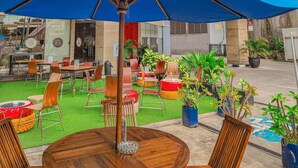 An outdoor seating area with wooden tables and chairs, a blue umbrella, and potted plants. - ibis Balikpapan (Balikpapan)