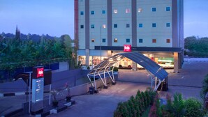 A modern hotel with a prominent "ibis HOTEL" sign, a covered entrance, and a landscaped area with plants. - ibis Balikpapan (Balikpapan)