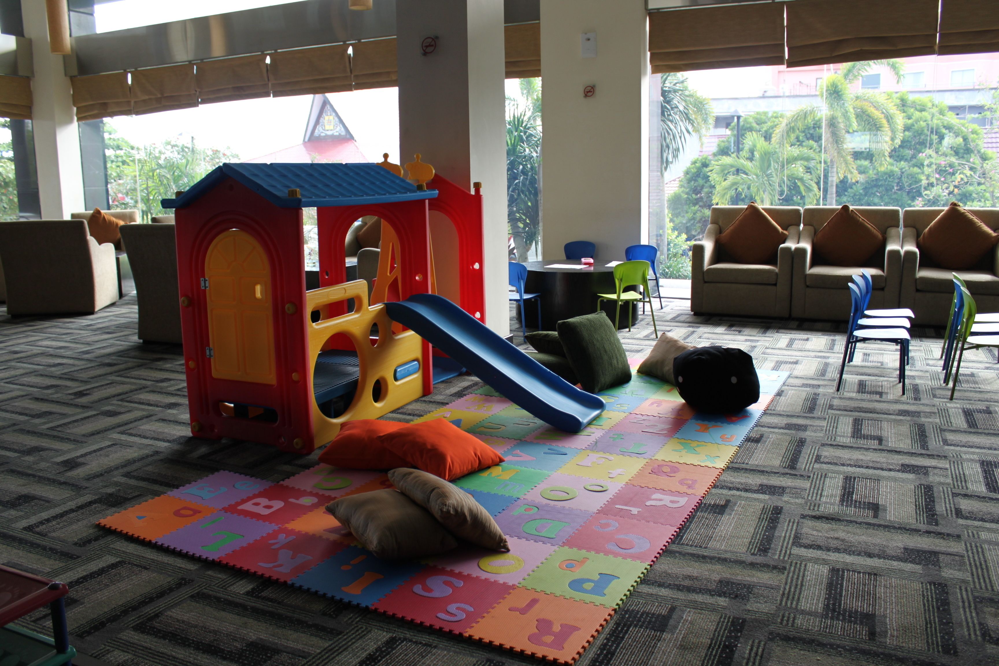 A play area with a slide and a playhouse, surrounded by seating and a carpeted floor.
