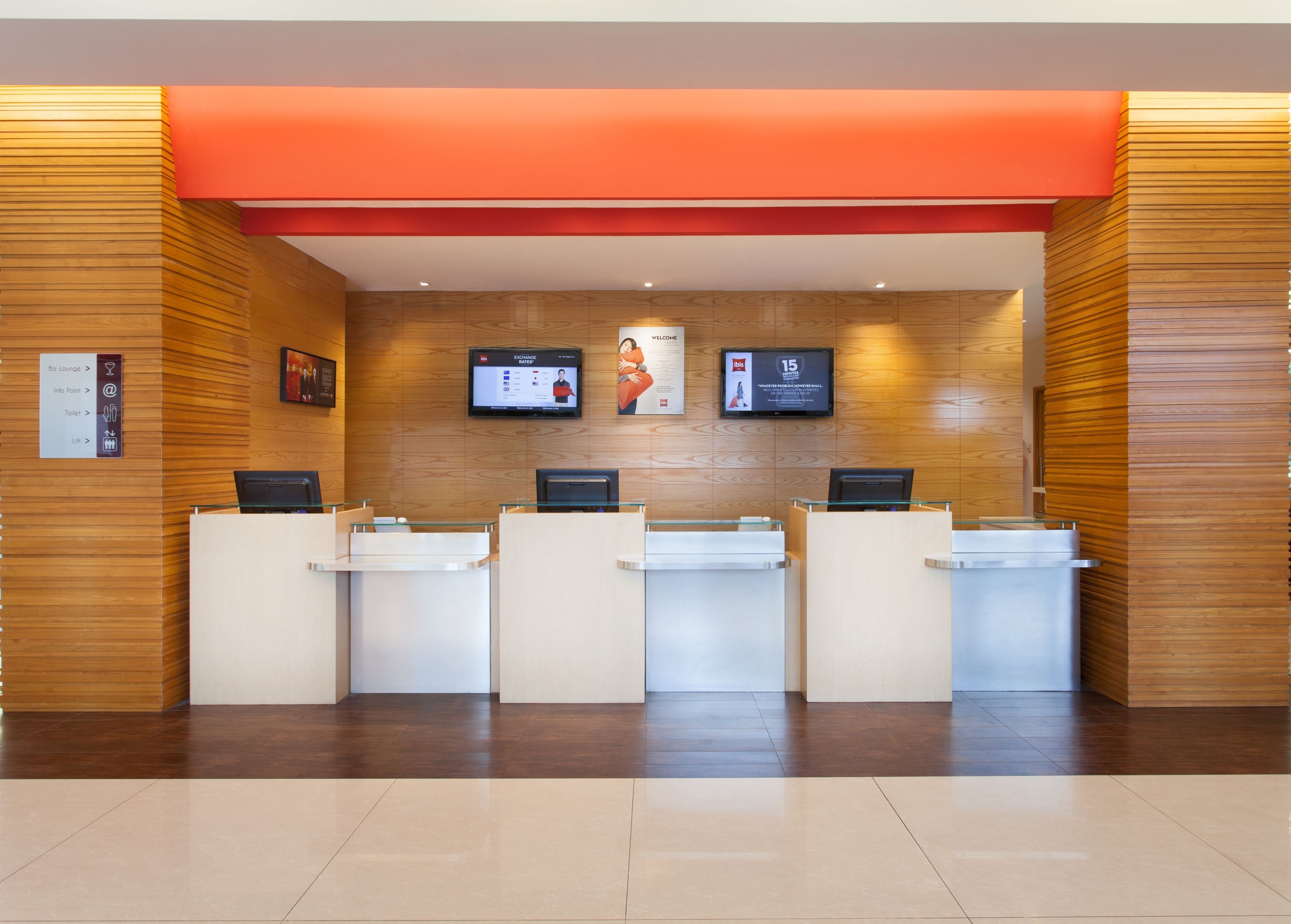 A reception area with a modern design, featuring a wooden wall, a red accent wall, and a digital screen displaying information.