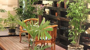 A wooden deck with a table and chairs, surrounded by potted plants and a decorative fountain. - ibis Balikpapan (Balikpapan)