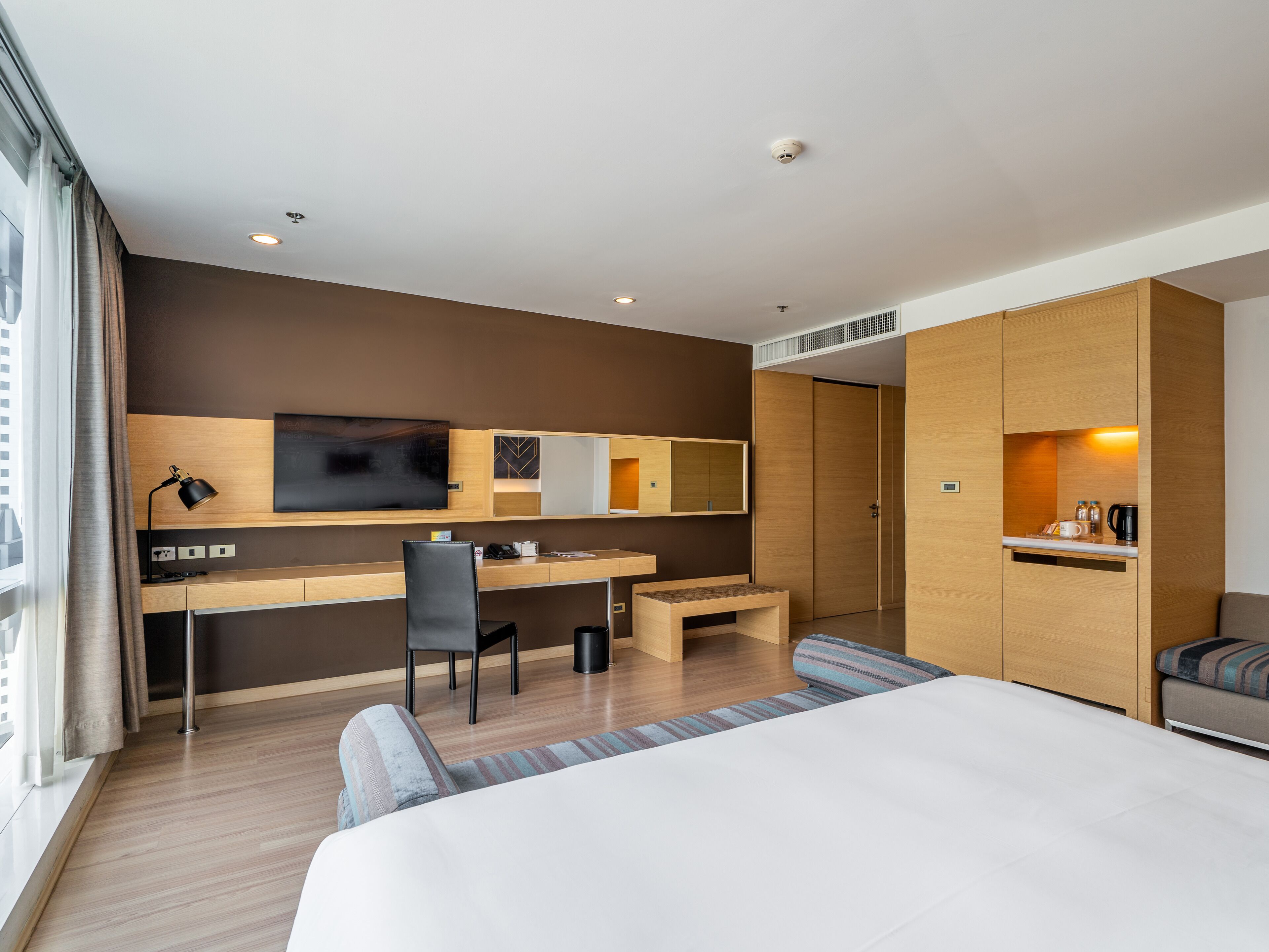 Een moderne hotelkamer met een groot bed, een bureau met stoel, een televisie en een kleine kitchenette.