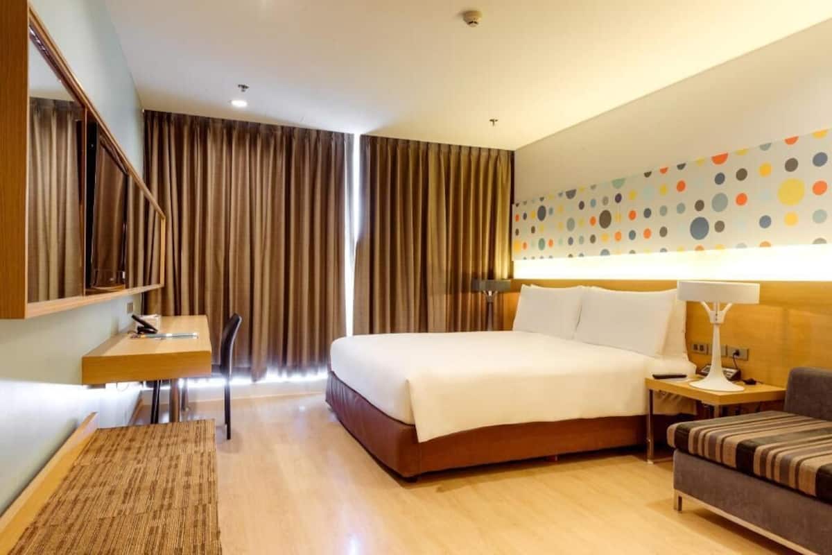 A hotel room with a bed, a desk, a chair, a sofa, and a wall with a polka dot pattern.