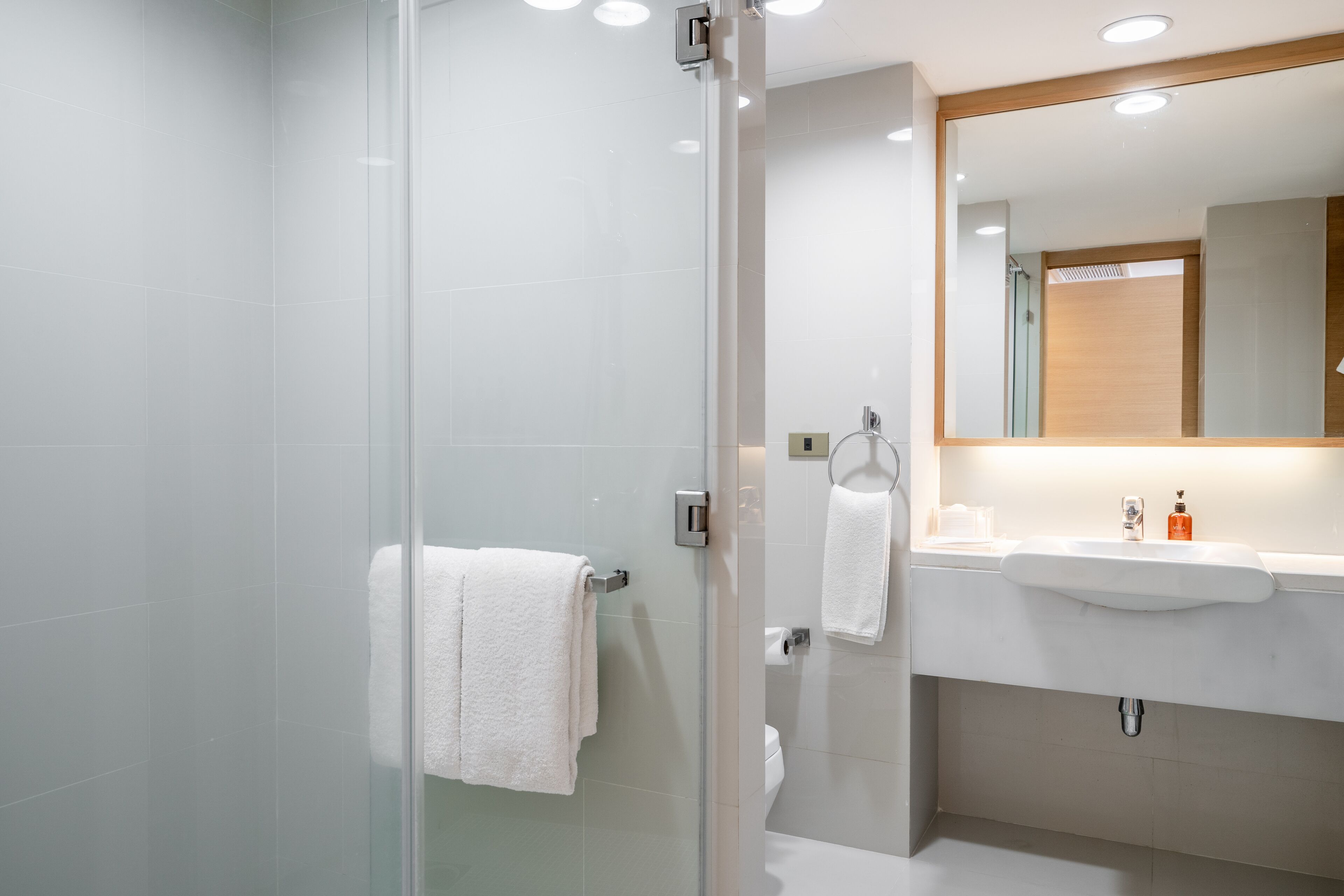 Un bany modern amb un plat de dutxa de vidre, un lavabo blanc i un mirall sobre el lavabo.