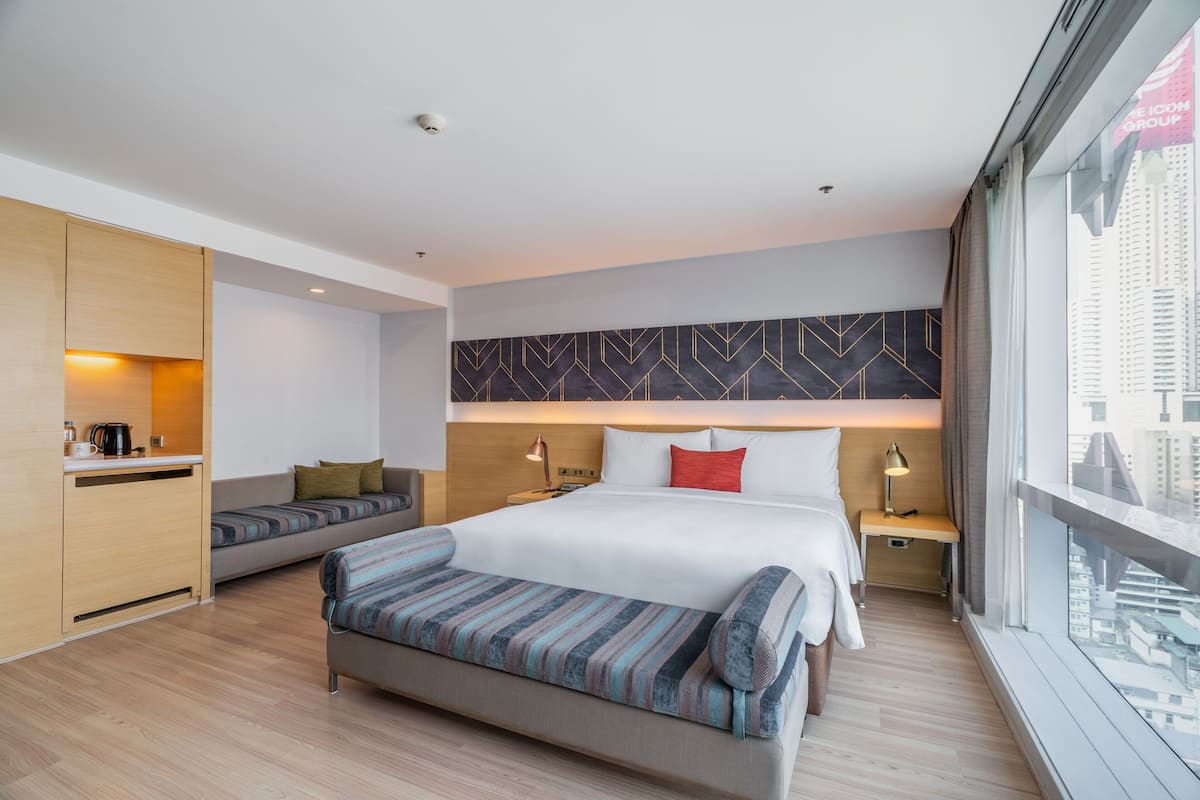 A modern hotel room with a large bed, a sofa, a small desk, and a view of the city.