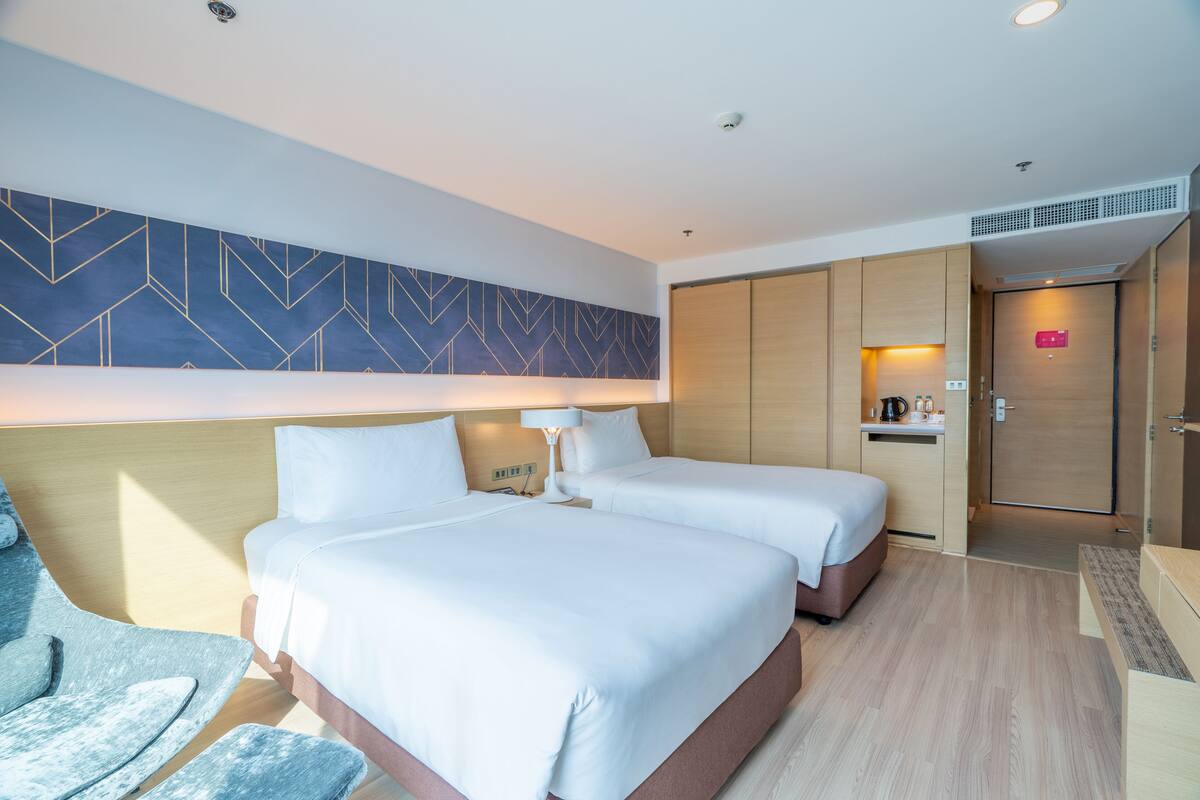 A hotel room with two beds, a desk, a chair, and a wardrobe.