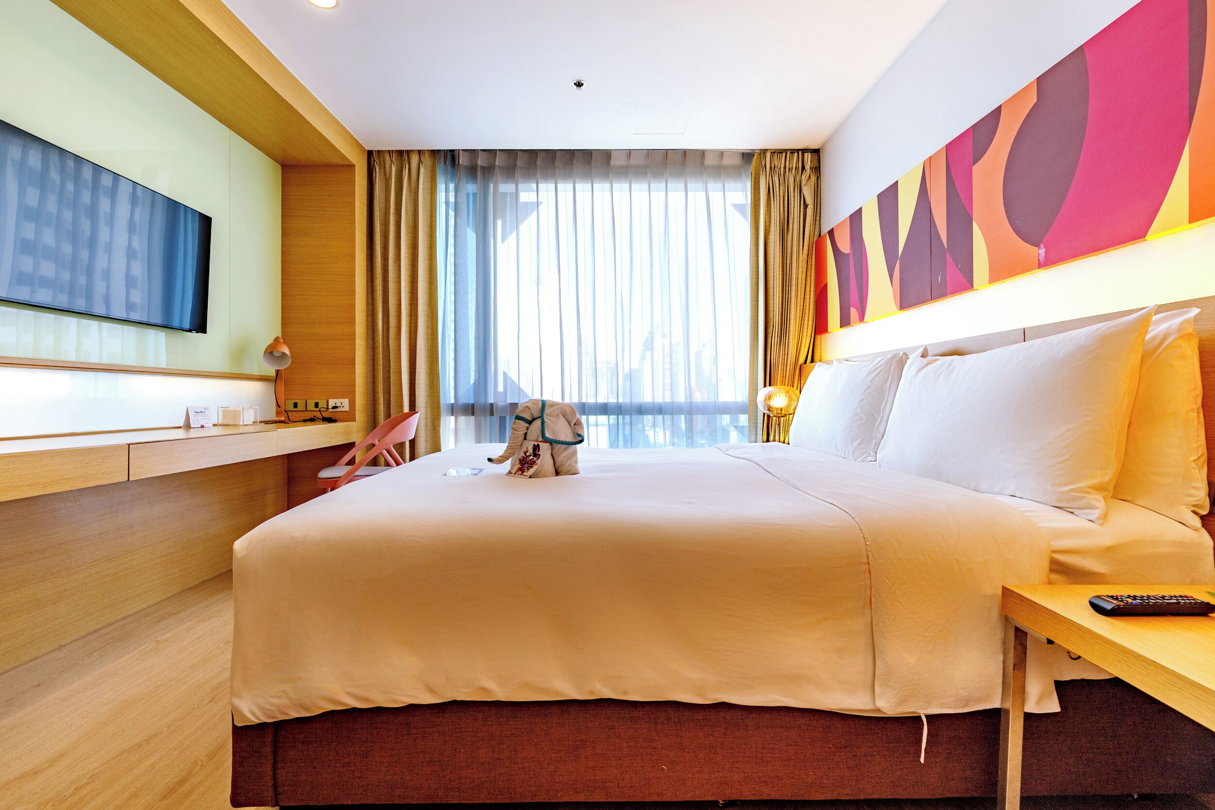 Una habitación de hotel con cama, escritorio, televisión, mesita de noche y ventana con cortinas.