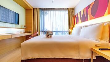 Una habitación de hotel con cama, escritorio, televisión, mesita de noche y ventana con cortinas.