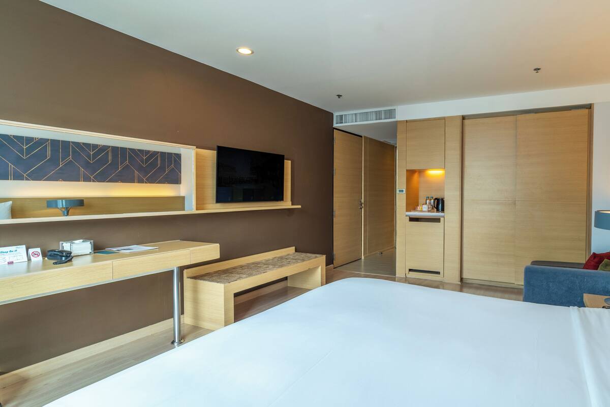 A hotel room with a bed, a desk, a television, a wardrobe, and a seating area.